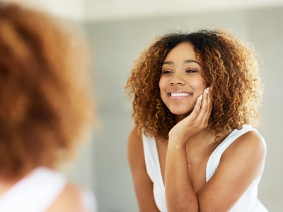 Woman admiring her flawless skin in the mirror after a vitamin C therapy session in Costa Mesa